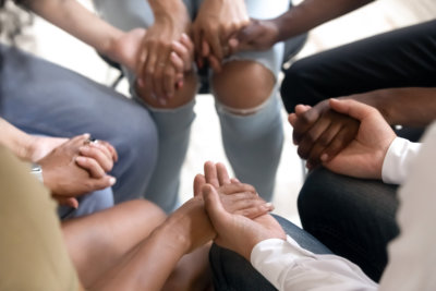 diverse people sitting in circle holding hands at group therapy